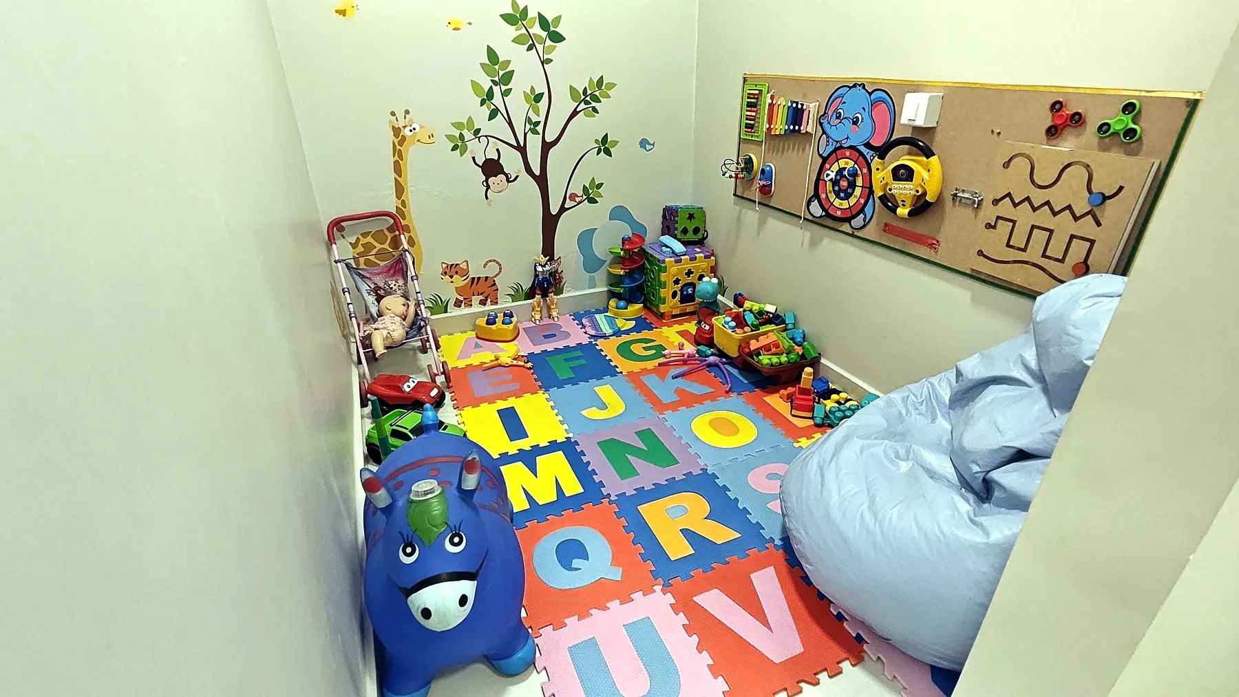 Sala lúdica da Progride, com tapete de letras, brinquedos e painel de atividades na parede